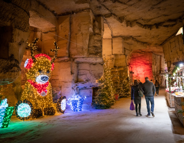 Shoppende mensen in Kerstmarkt gemeentegrot passeren kerstkraampjes en grote verlichte beer